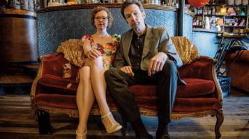 Image of musical duo Birdcode sitting on a red couch in an empty bar.