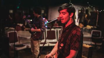 The lead singer of the Couchsleepers sings into a microphone, light by a red stage light.