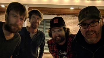 The John Daly band members stand and lean in towards each other.