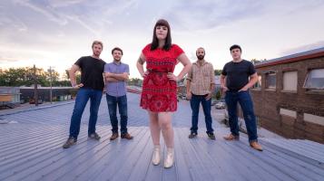 The lead singer of the Red Newts, is flanked by the rest of the band members, standing on a rooftop.