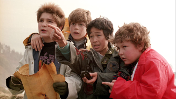 A still from The Goonies, showing four boys standing closely together, one holding a treasure map and one points ahead.