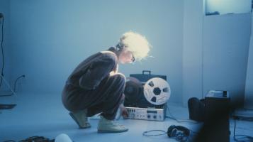 An still from Sisters with Transistors, showing a woman kneeling in front of sound equipment.
