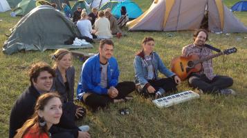 the band with instruments sitting in a field with camping tents in Finland