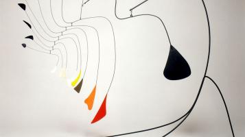 An alexander Calder mobile sculpture with a thin curvilinear black metal stand, and nested curved arms ending in colorful metal petals.