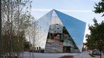 An angular building covered with reflective glass windows, with birch trees and a city street in the foreground.