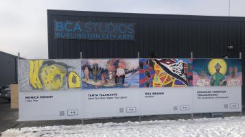 A photograph of a temporary wall covered in colorful murals, in front of dark gray building with corrugated metal siding and a blue sign that reads BCA Studios Burlington City Arts.