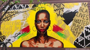 A mural featuring the head and shoulders of a dark skinned woman wearing large hoop earrings, on a patchwork background with swathes of yellow, red, green, geometric black and white kente print and Black Lives Matters signs