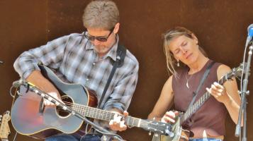 Dana is playing acoustic guitar and Beth is playing a banjo onstage, both have their eyes closed