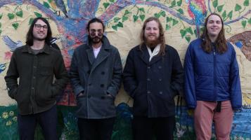 4 band members stand in front a a painted tree mural