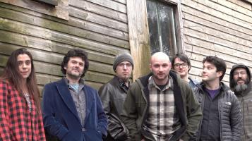 Member of band pose in front of a knotty wood building