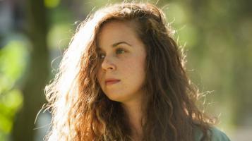 A headshot of a light skinned woman with dark red hair