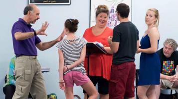 A woman wearing an orange tee shirt smailes and talks to a group of people