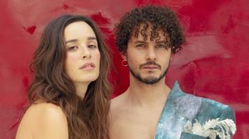 A woman and a man with curly dark hair against a painterly red backdrop