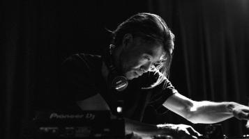 A black an white image of a man wearing a black tee shirt leaning over a turntable