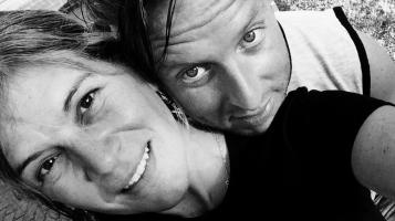 A black and white close up image of a light skinned woman and man. The man rests his chin on the woman's shoulder