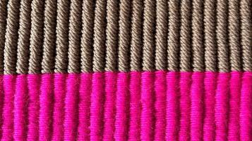 a photograph of a close up of a piece of textile art comprised of tightly woven ribs of thread. The top half are light brown and appear to be made of jute and the bottom half are bright magenta.