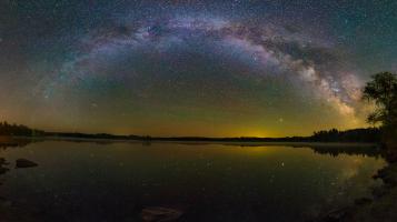 A long exposure color photograph of a nebula over a lake