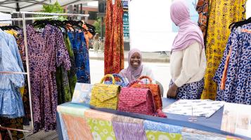 A woman with a headscarf in a market book smiling at the camera