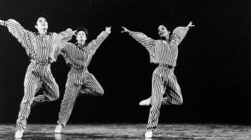 A black and white image of three dancers with one leg up and their arms extended