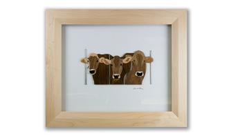 An image of a front view of three cows made out of wood within a wood shadow box