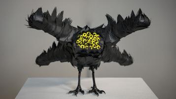 A black bird like sculpture with many yellow eyes standing on a white pedestral.