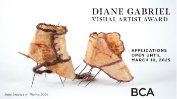 A small sculture created by Diane Gabriel depicting handmade tan baby slippers with the soles made out of tiny needles