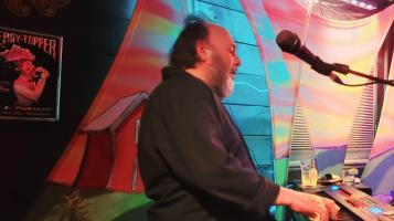 man with bright fabric behind him singing into mic.