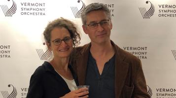 two people standing infront of a wall with the graphic for vermont symphony orchestra behind them