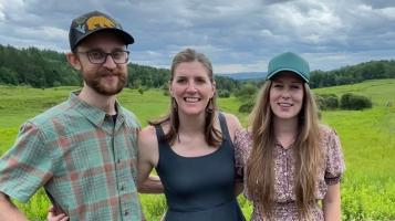 Three people standing outside with a field behind them