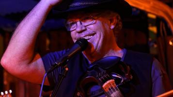 a man with glasses smiling into a mic with pink light