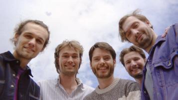 five guys standing around a camera looking down with a sky background.
