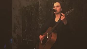 a person singing into the mic with a dark background holding a guitar