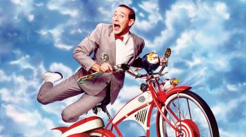 Pee-Wee Herman gleefully holding onto his precious bike as he soars through the cloudy blue sky
