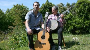 two people sitting outside on a sunny day playing guitar and banjo.