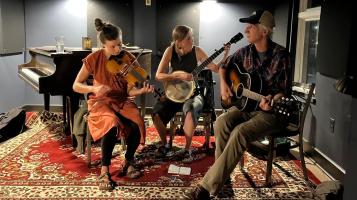 three people playing music in a grey room with a red rug