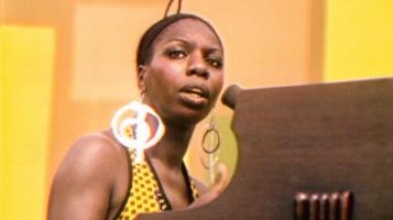 A beautiful Nina Simone sits at a piano and stares out into the crowd