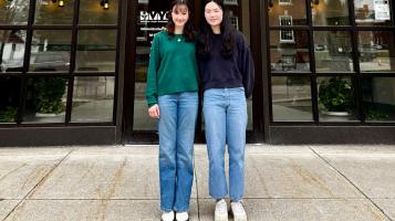 two teenage girls standing on the sidwalk facing the camera