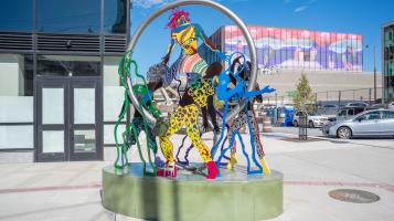 A photo of Dance in Place an outdoor public sculpture in Burlington, VT that consists of colorful intertwined steel cutouts of people dancing within a suspended steel ring