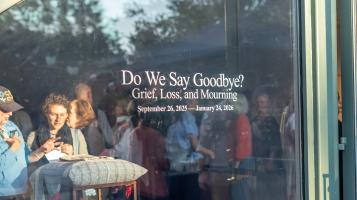 Image of a glass gallery entrance with the words "Do We Say Goodbye? Grief, Loss, and Mourning. September 16,2025-January 24,2026" with people in mingling inside.