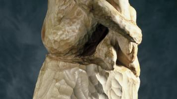 Birch wood sculpture of a woman, knees pulled up to her chin. 