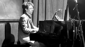 A stylized balck and while photo of a man with dark hair playing the piano