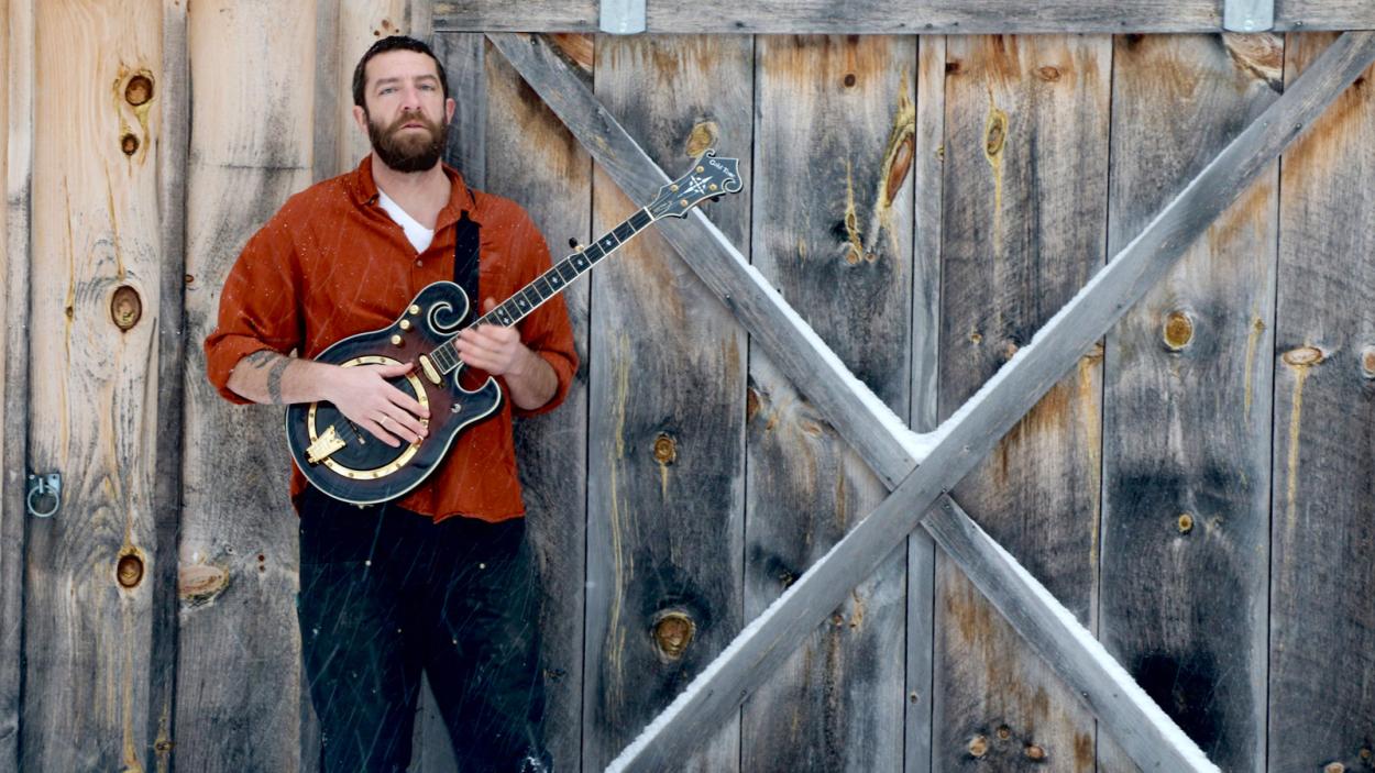 artist holding a banjo in front of wooden barn door