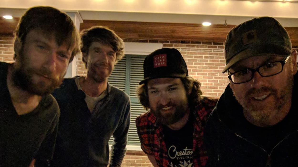 The John Daly band members stand and lean in towards each other.