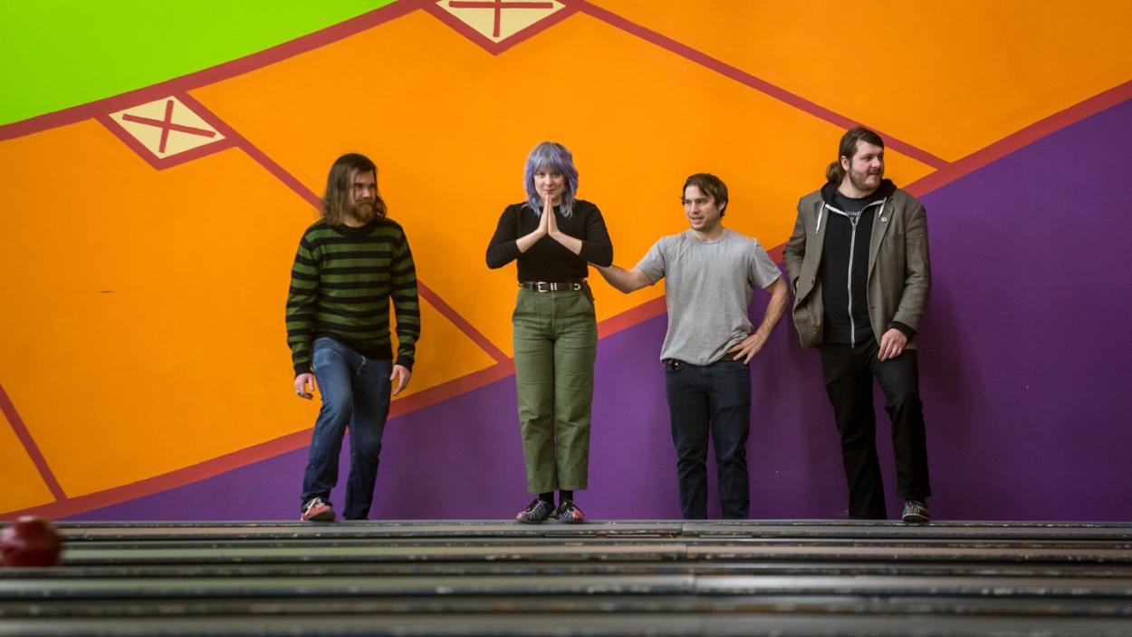 The four members of the Clever Girls stand in front of a brightly painted mural at the top of a et of stairs.