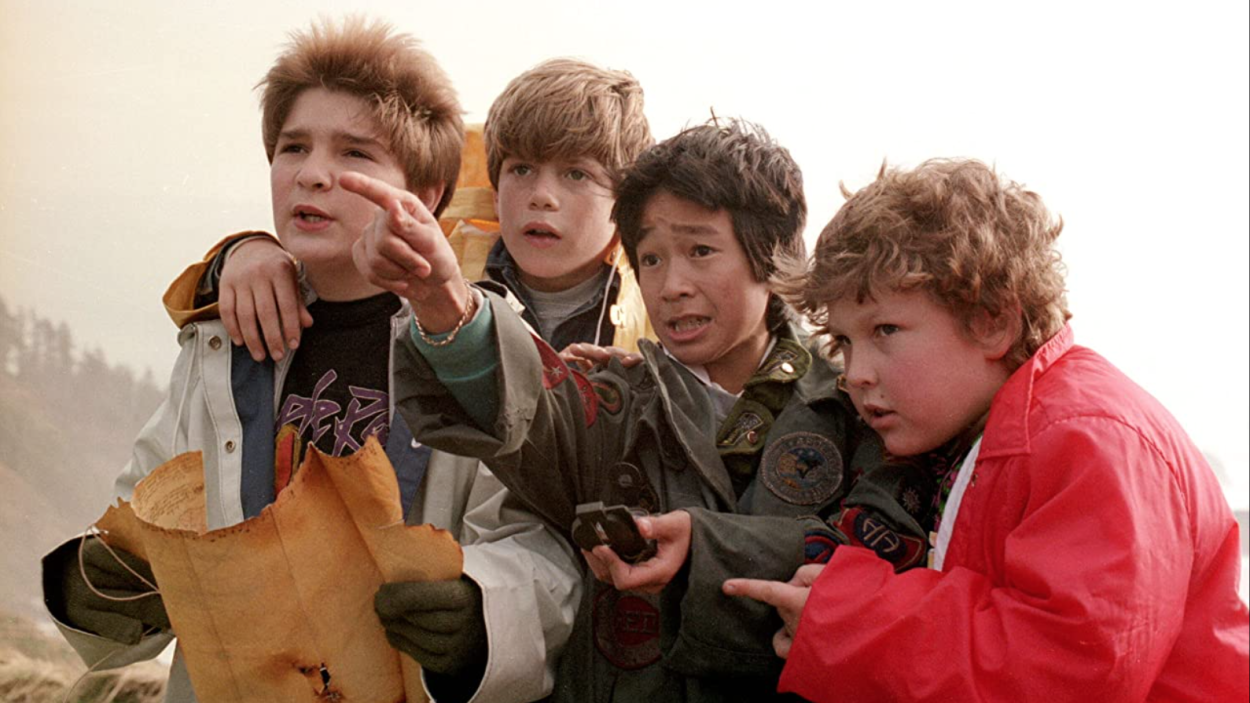 A still from The Goonies, showing four boys standing closely together, one holding a treasure map and one points ahead.