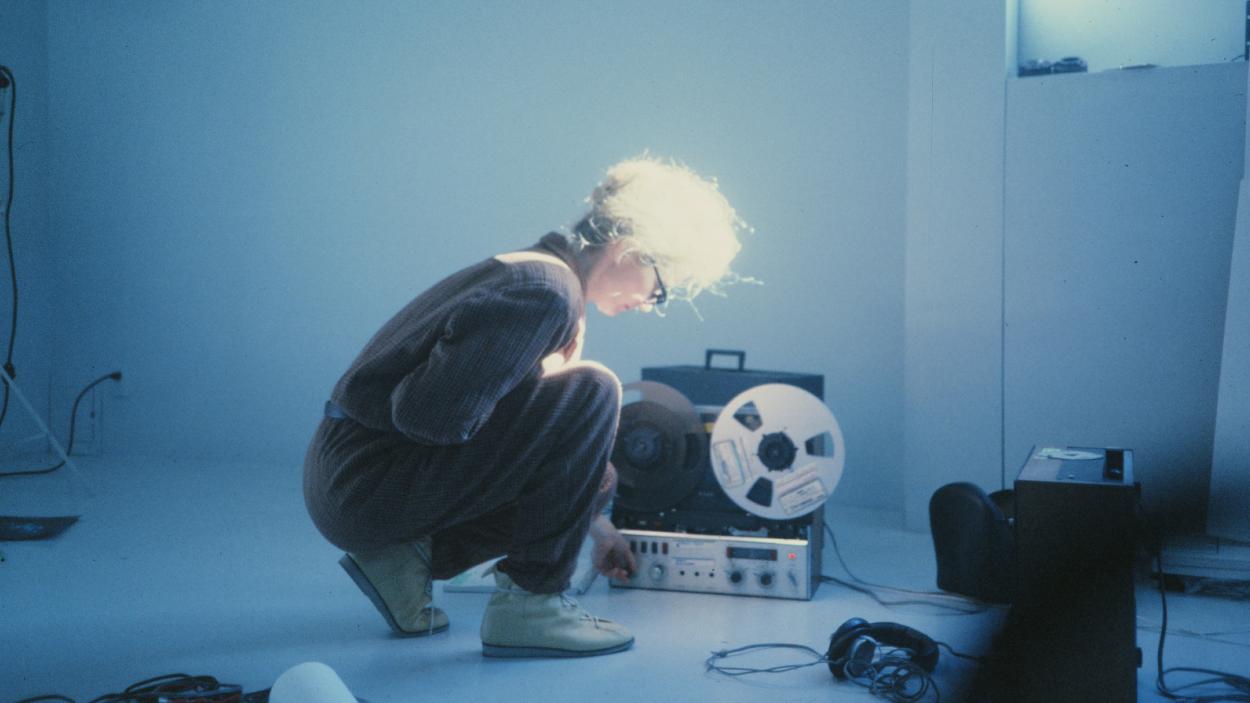 An still from Sisters with Transistors, showing a woman kneeling in front of sound equipment.