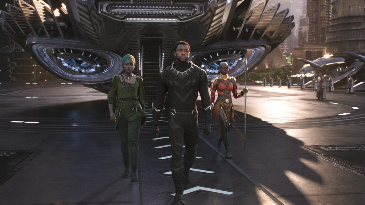 A still from Black Panther showing Prince T'Challa walking away from a high tech plane's staircase flanked by two women.
