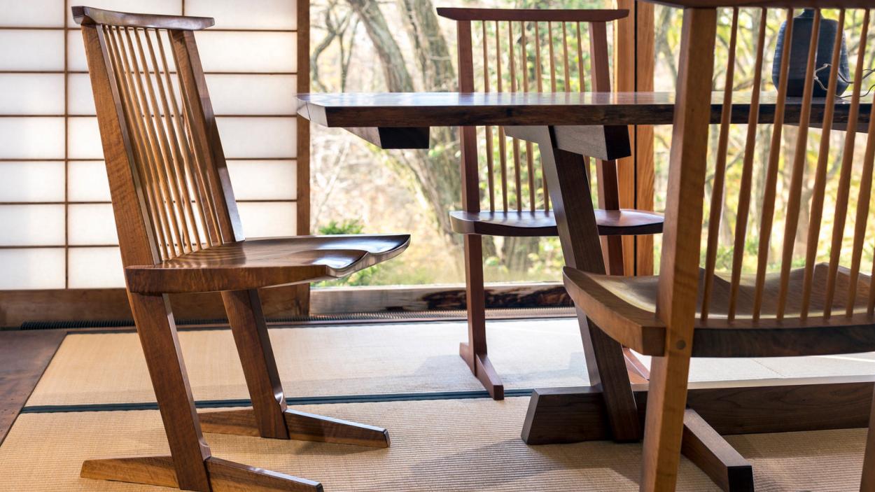 Angular spindle back wooden chairs are gathered around a table with sloping legs.