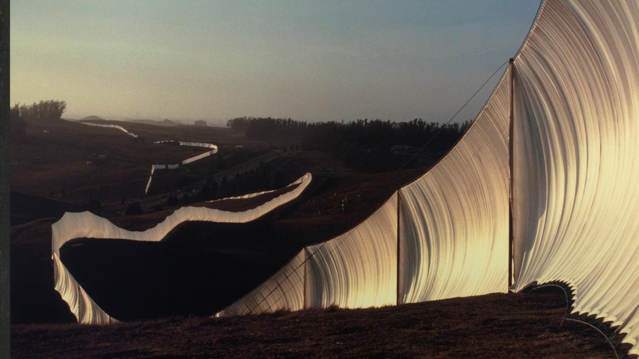 A photograph of Christo and Jean Claude's installation piece, a fence of white fabric snaking across the hills of northern California