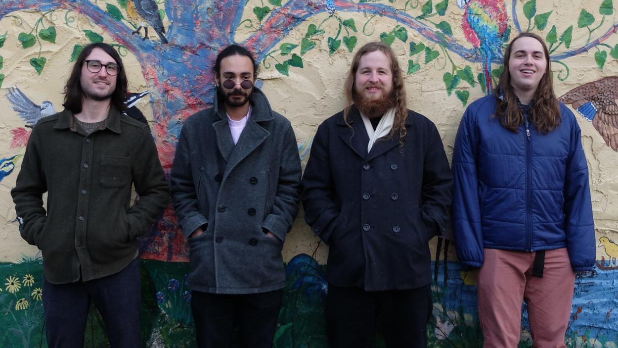 4 band members stand in front a a painted tree mural